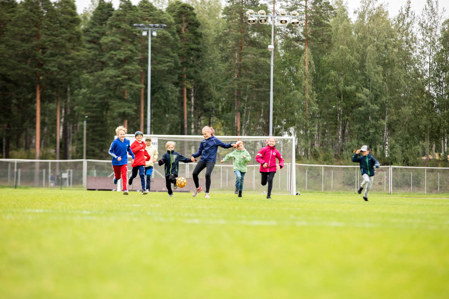 Koululaiset pelaavat jalkapalloa kentällä.